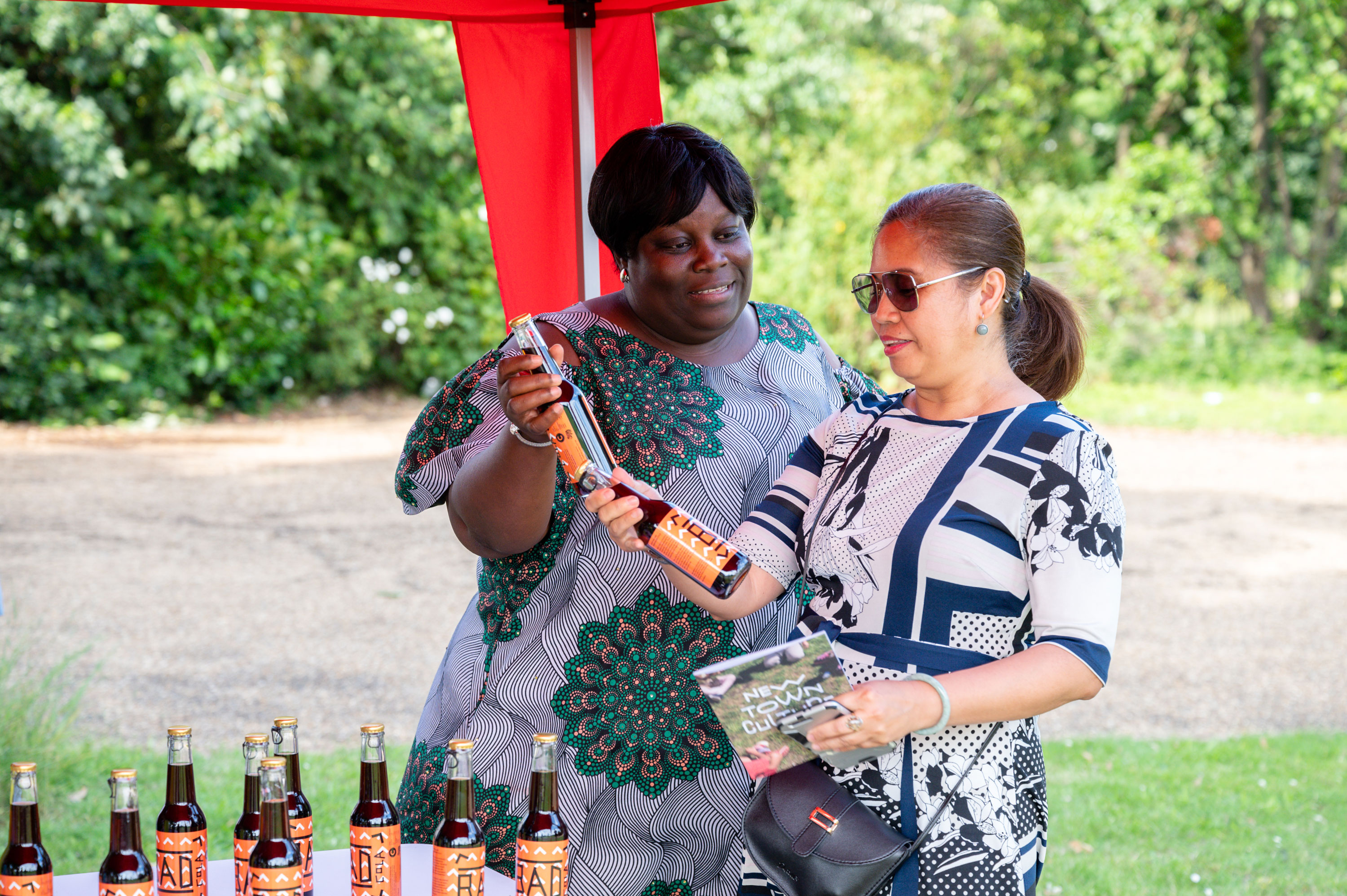 Two women smiling and looking at drinks bottles outside and underneath a gazeboo