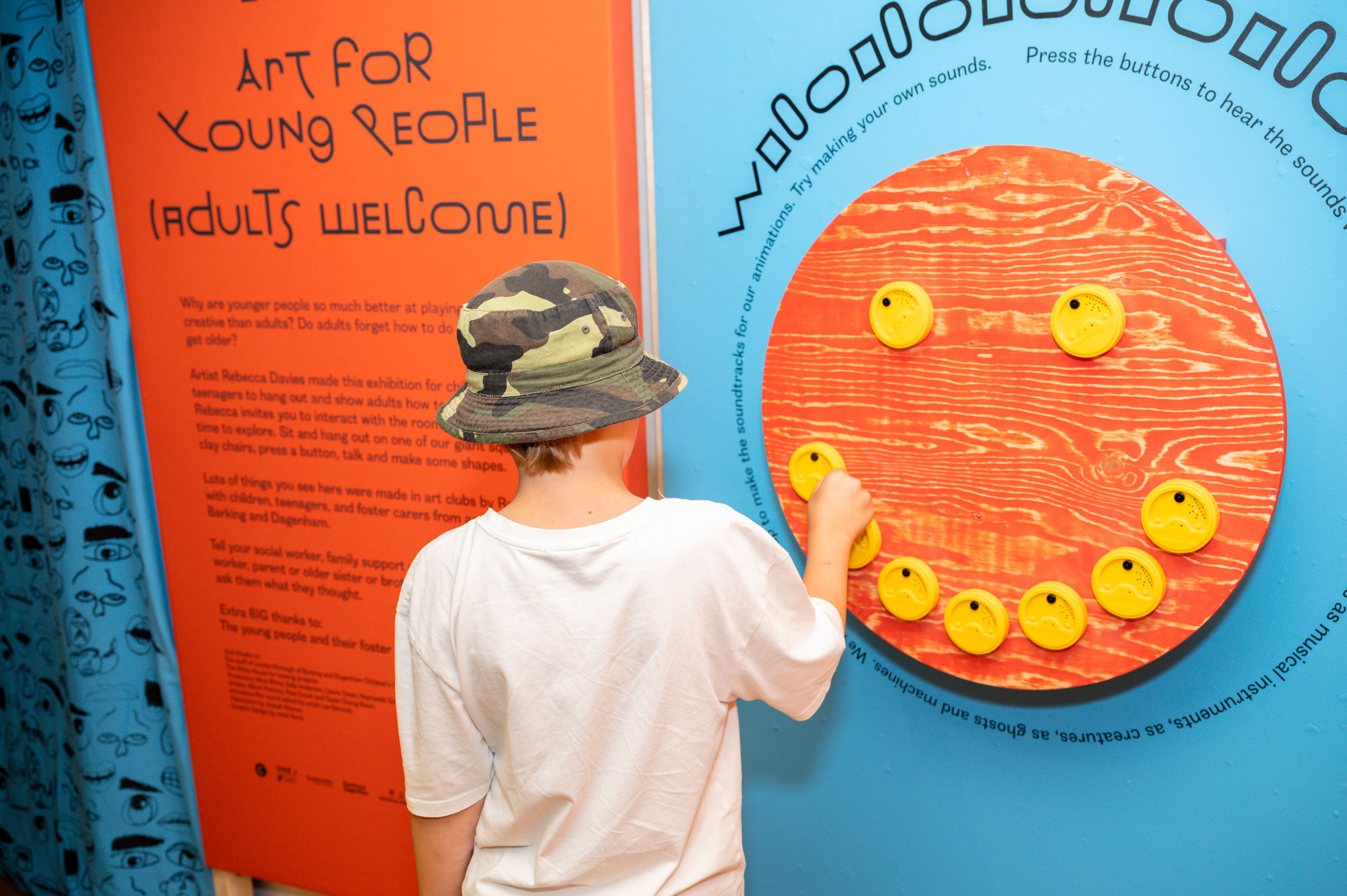A young boy playing with a yellow button displayed on a big red circle placed on a blue wall