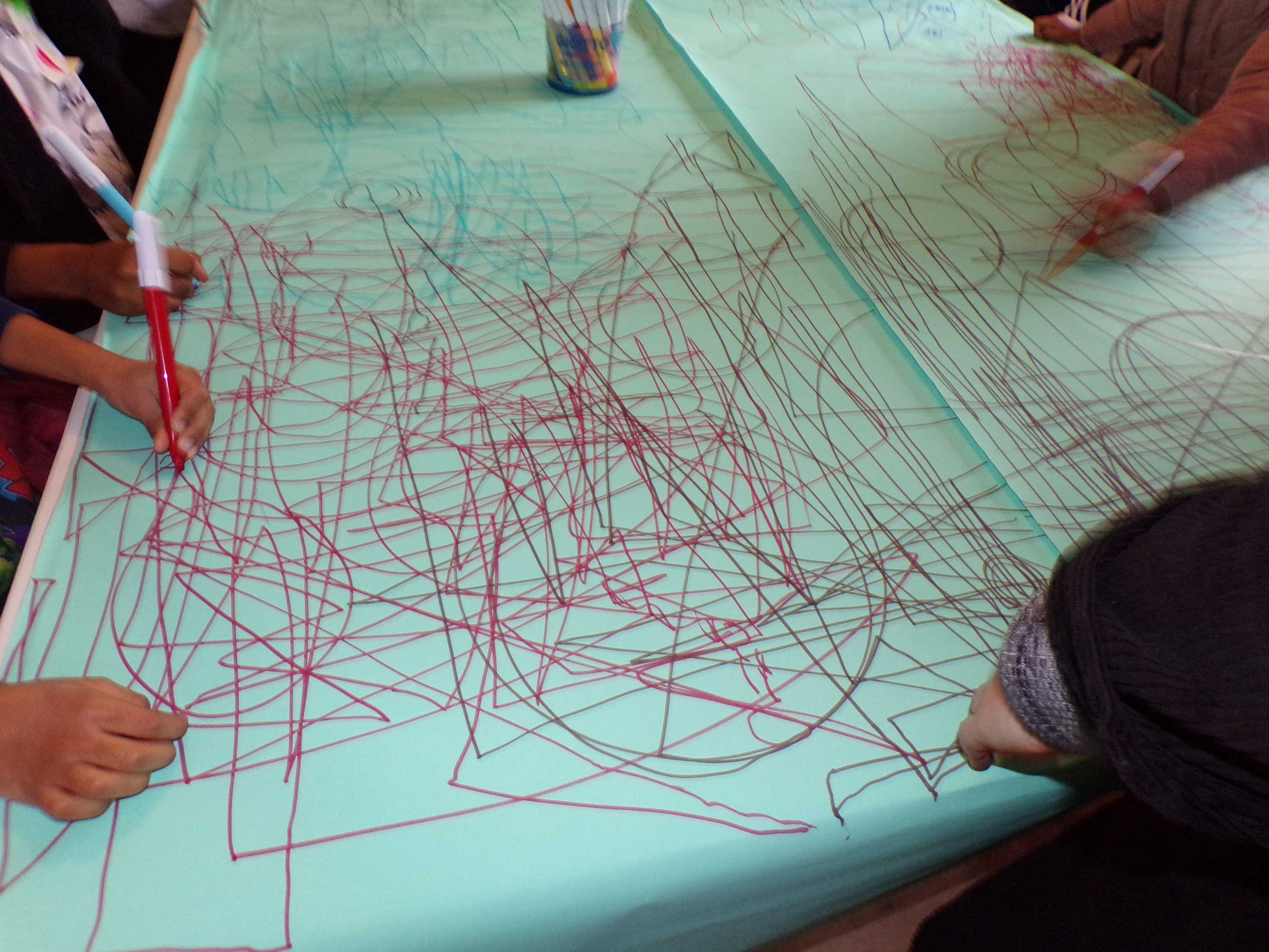 A group of participants creating patterns and mark making using red pens on a green paper