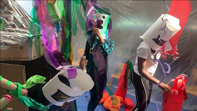 Moving image still of three participants wearing paper masks exploring the hanging and static materials