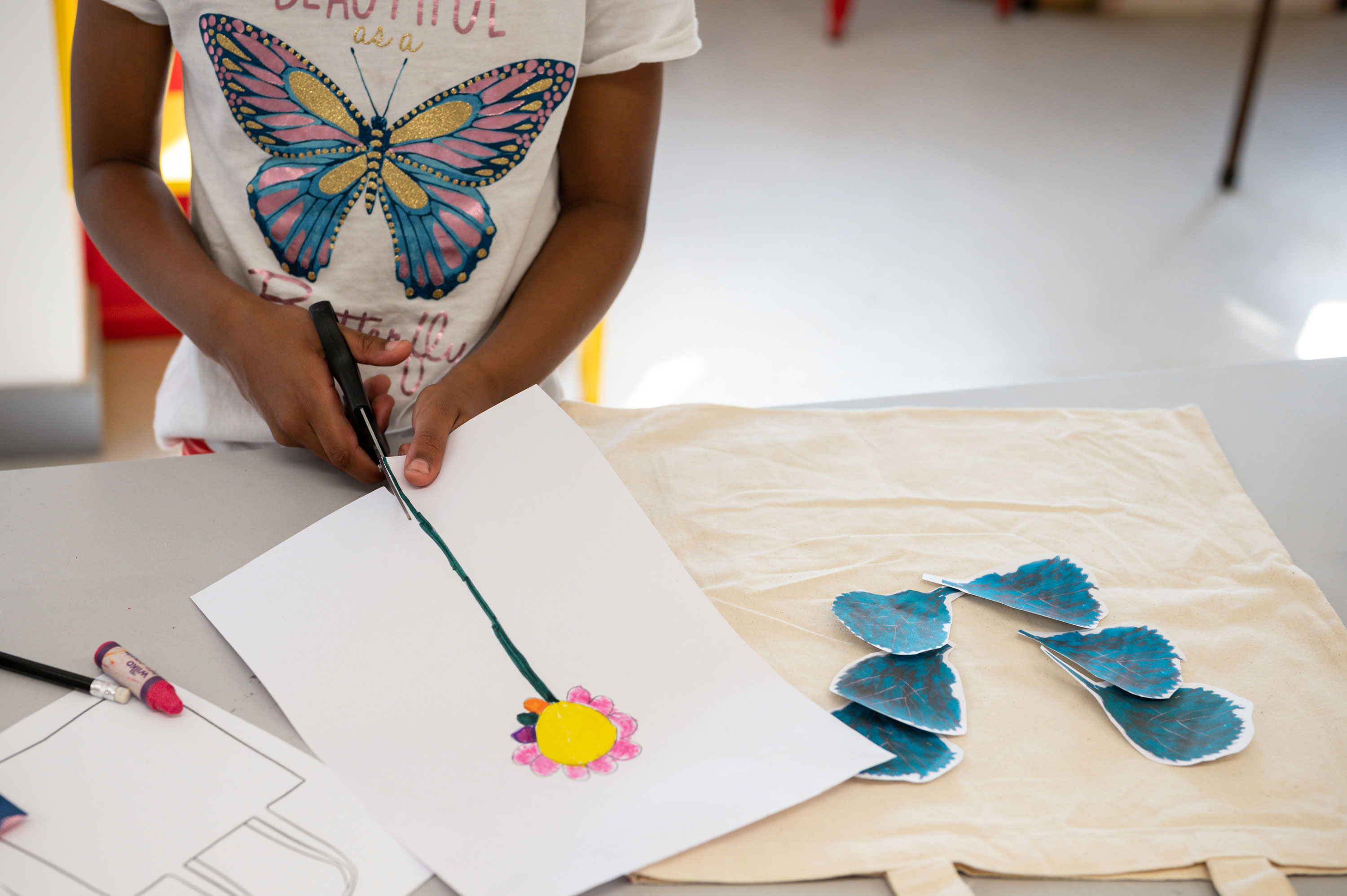 A young person using scissors to cut out a drawing of a long green, pink and yellow flower