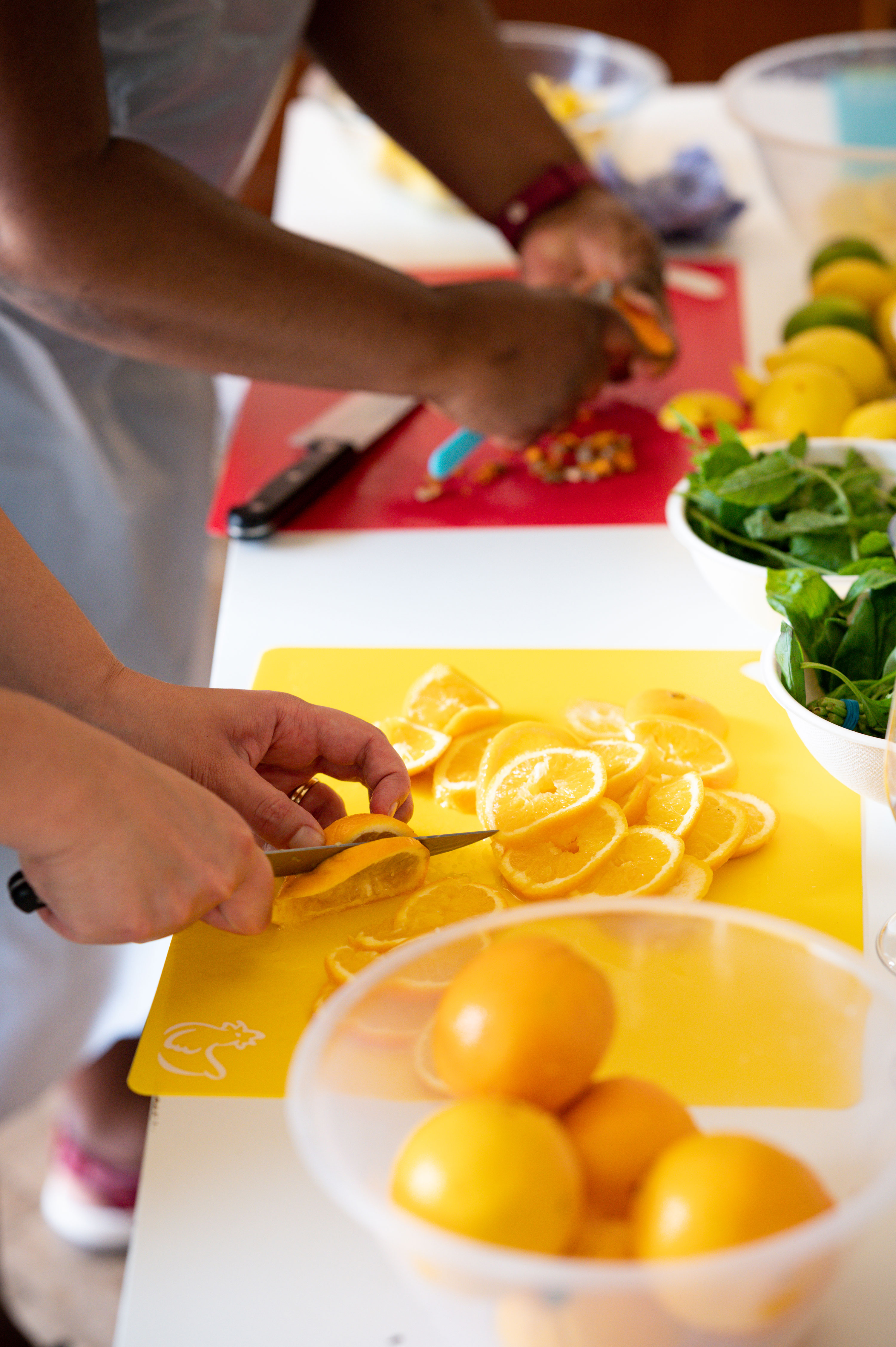 Two people using a knife to cut oranges into slices