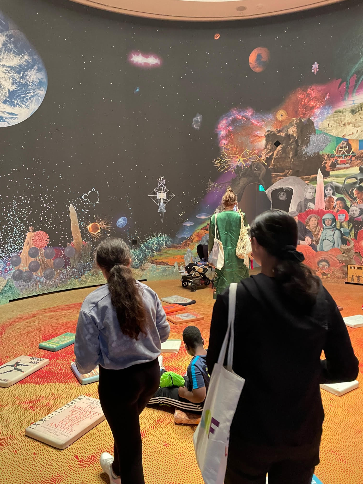 Group of young people standing, sitting and walking in a room with a huge image of earth and outer space on the wall