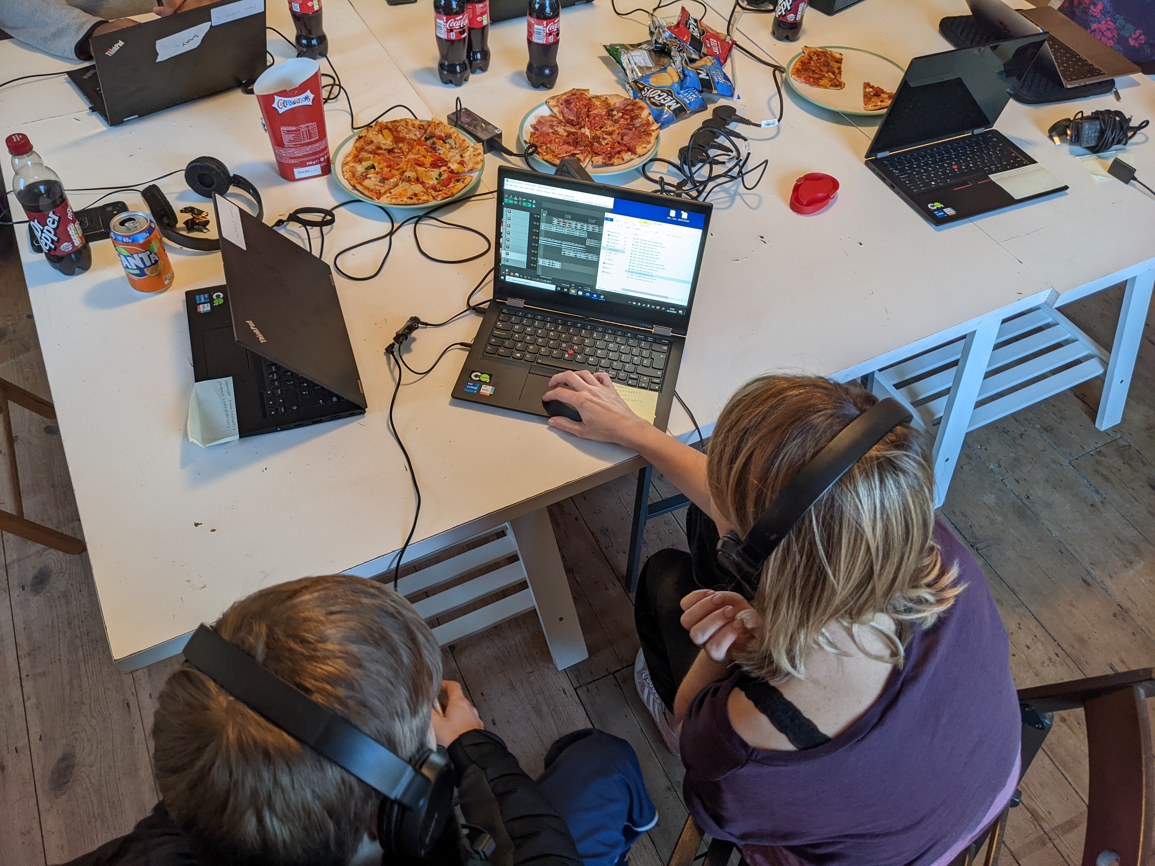 2 people editing sound at a computer with pizza and cola on the table next to them